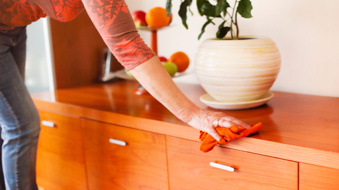 Une femme nettoie un meuble en bois avec des gants orange, protégeant ainsi les surfaces pour une propreté durable.